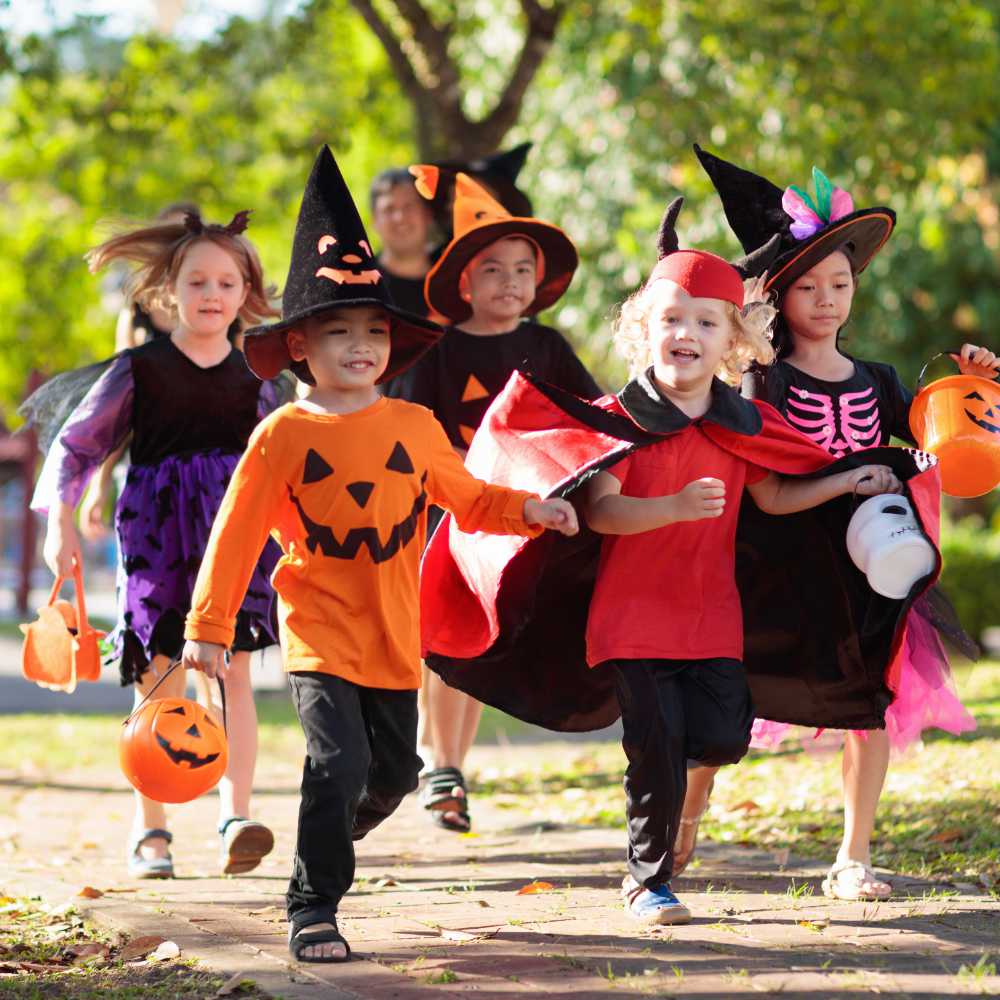 Kids trick or treat. Halloween fun for children. Child in Halloween costume. Mixed race Asian and Caucasian kids and parents trick or treat on street. Little boy and girl with pumpkin lantern and candy bucket. Baby in witch hat. Autumn holiday fun.